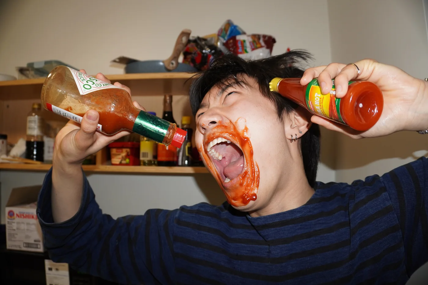 Sauce-covered hands holding a hot sauce bottle