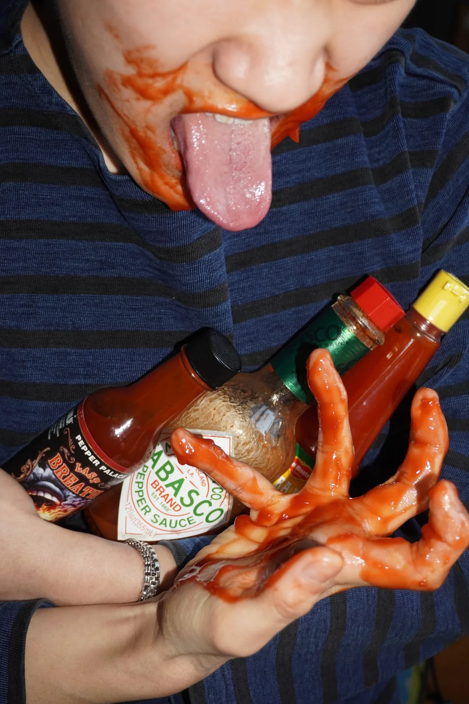 Sauce-covered hands gripping a bottle of hot sauce