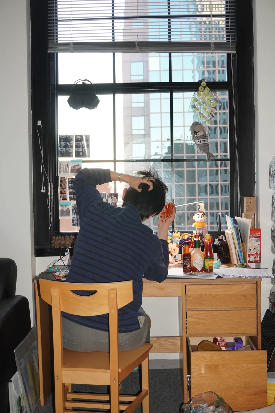 Sitting at a desk by a window, tipping back a bottle