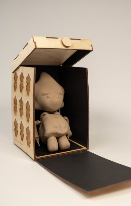 The wooden Zeno box standing upright with a patterned side panel and the figure seated in its doorway
